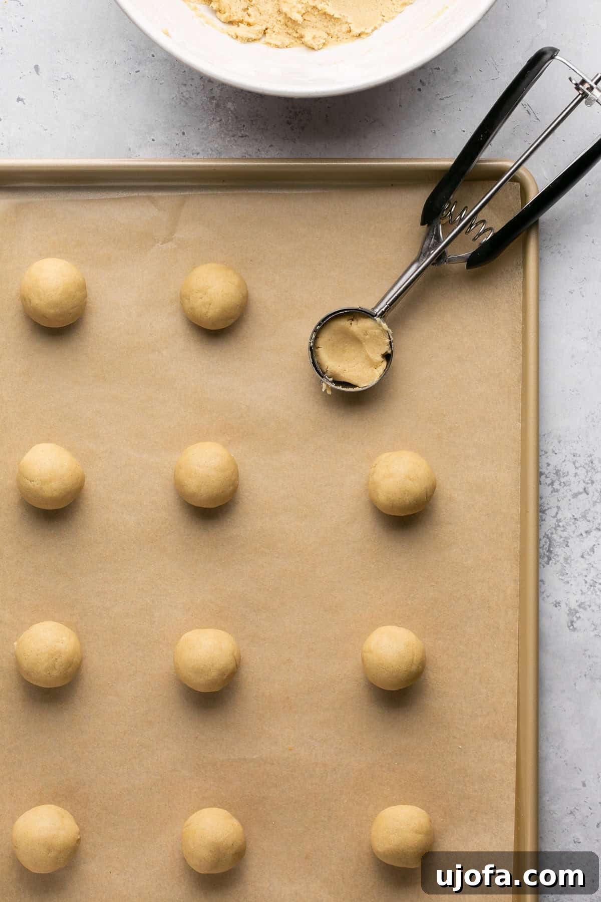 Uniform balls of cookie dough scooped onto a parchment-lined baking sheet, with a cookie scoop nearby.