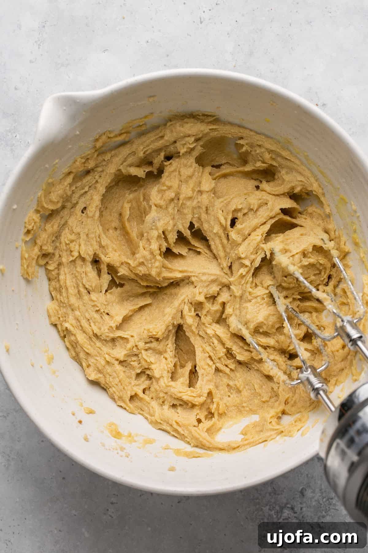 Well-mixed eggs, sugars, and butter in a white bowl, smooth and creamy.