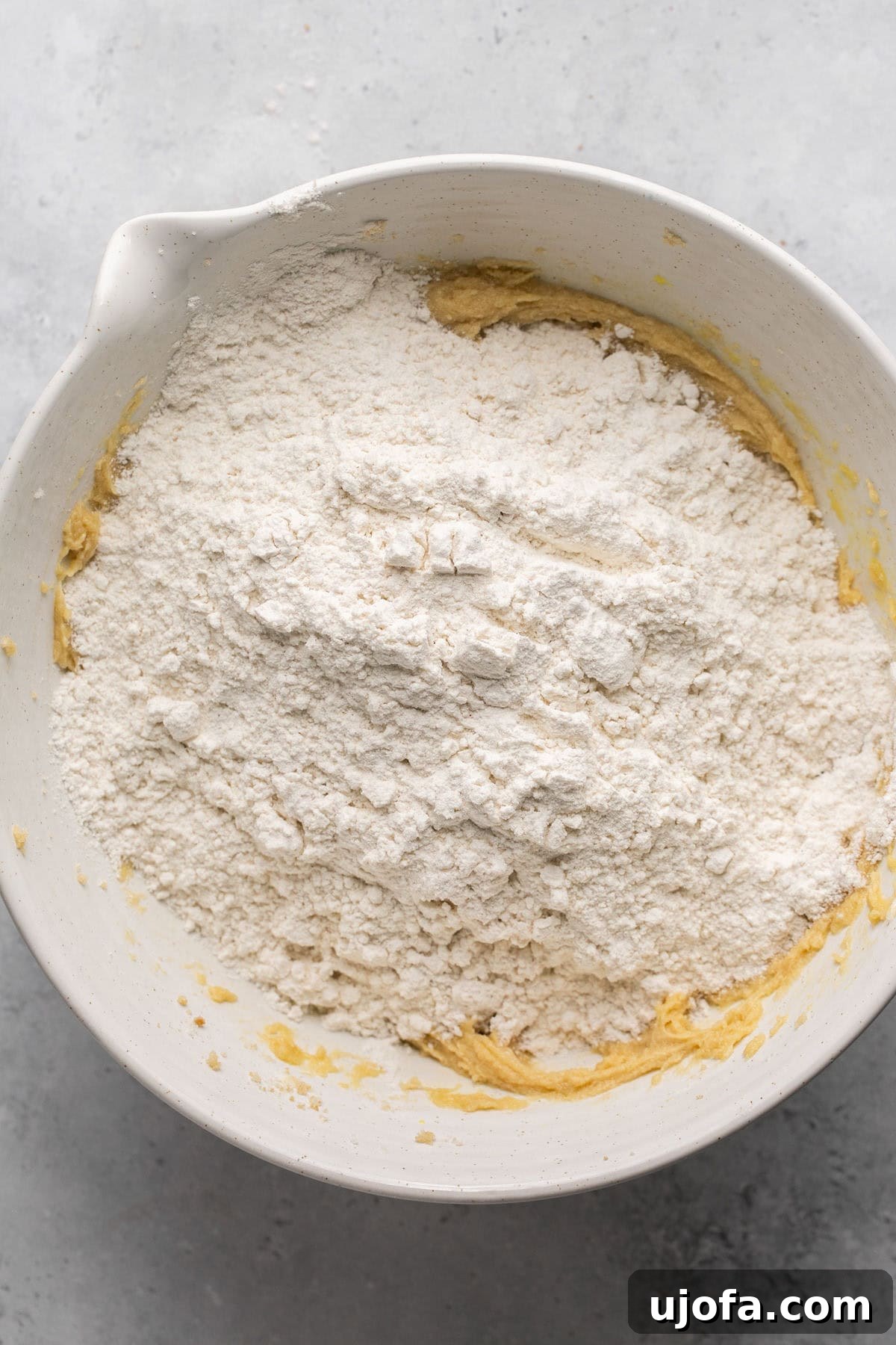 Dry ingredients being added into the wet mixture of sugar, egg, and butter in a bowl.