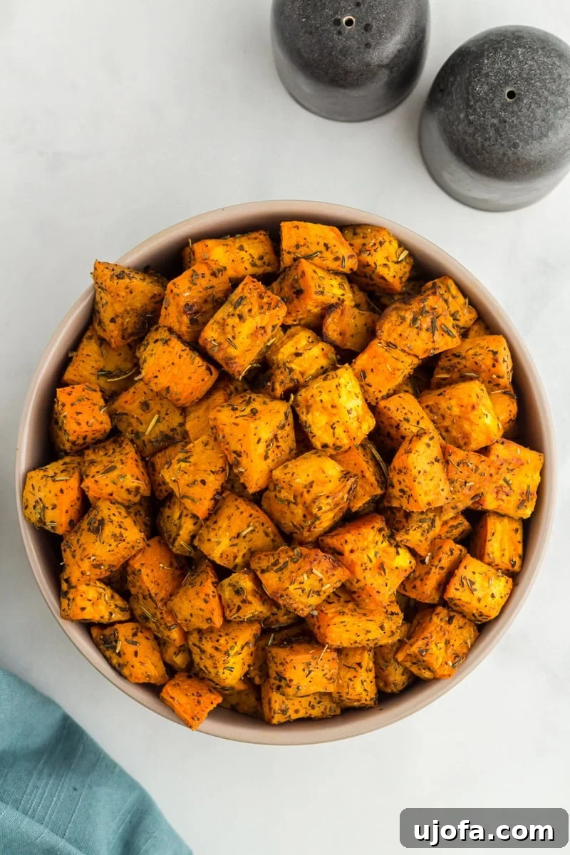 Golden Roasted Sweet Potatoes 2 Bowl filled with golden roasted sweet potato cubes seasoned with herbs, placed on a light background with salt and pepper shakers nearby.