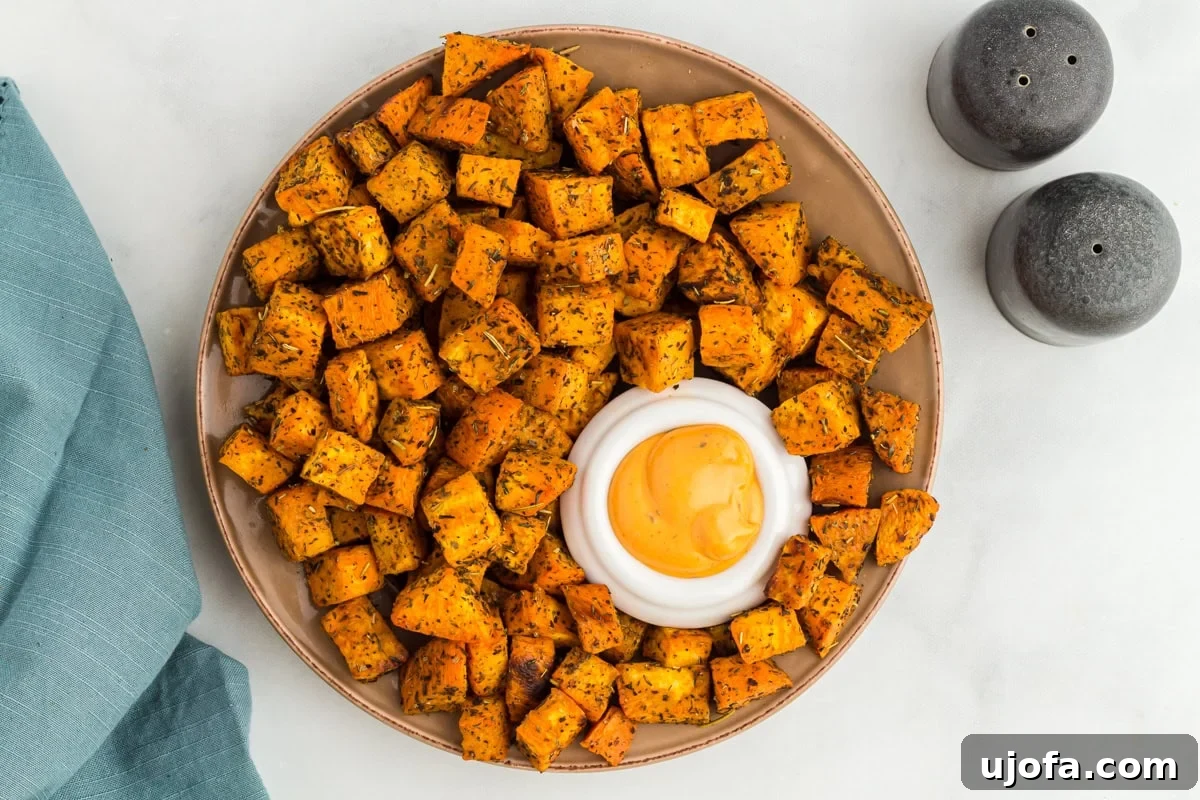 Golden Roasted Sweet Potatoes 10 A round serving plate filled with roasted sweet potato cubes, centered around a small bowl of creamy dipping sauce, with salt and pepper shakers nearby.