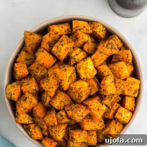 Bowl filled with golden roasted sweet potato cubes seasoned with herbs, placed on a light background with salt and pepper shakers nearby.