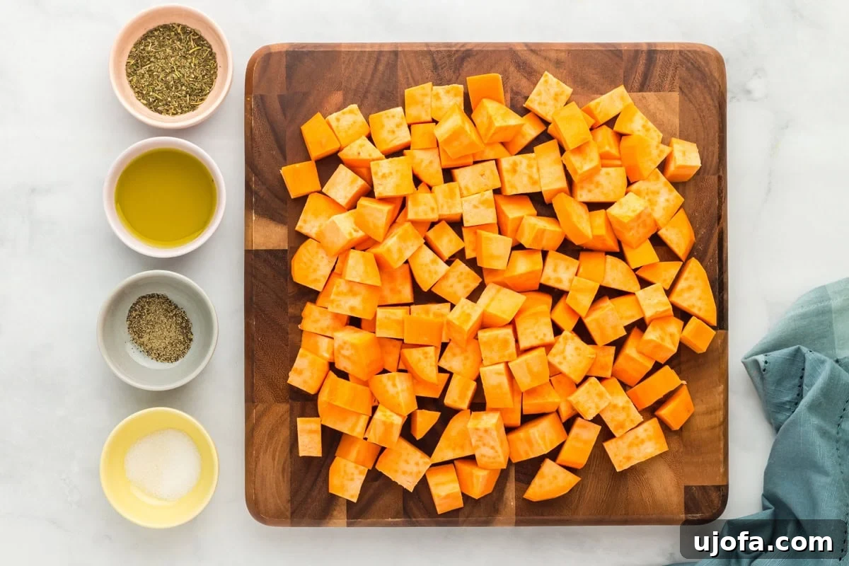 Golden Roasted Sweet Potatoes 5 Cubed sweet potatoes on a wooden cutting board with small bowls of olive oil, Italian seasoning, salt, and black pepper arranged beside them.