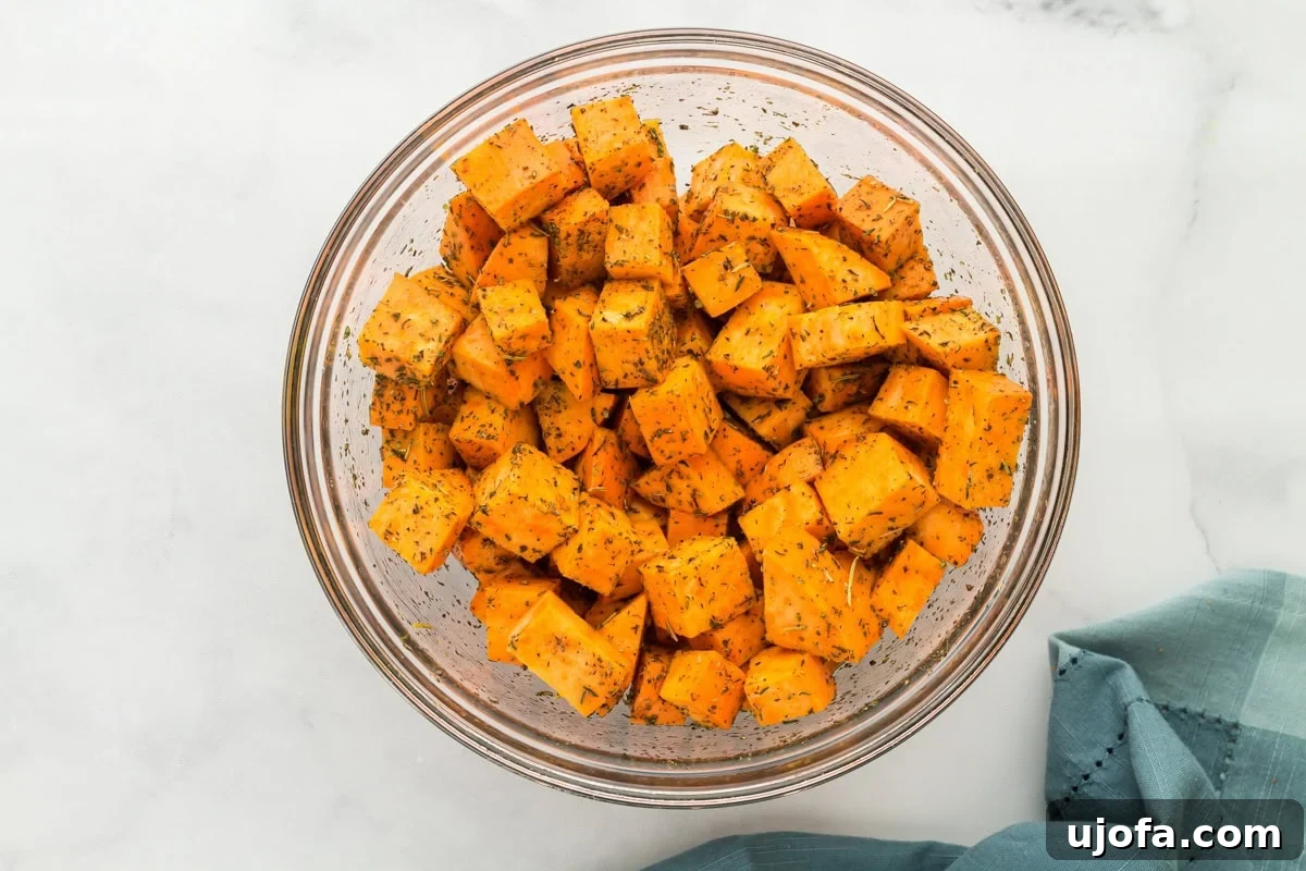 Golden Roasted Sweet Potatoes 6 Raw sweet potato cubes in a large glass mixing bowl, coated with olive oil, Italian seasoning, salt, and pepper.