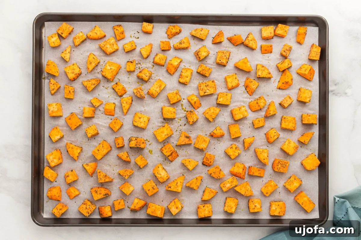 Golden Roasted Sweet Potatoes 7 Seasoned sweet potato cubes spread out evenly on a parchment-lined baking sheet, ready to roast.