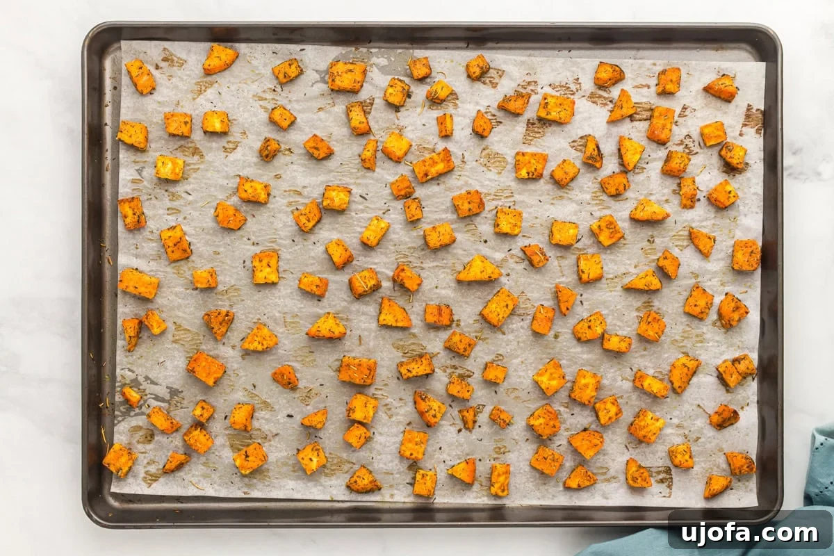Golden Roasted Sweet Potatoes 8 Sweet potato cubes on a baking sheet after roasting, lightly browned and starting to crisp around the edges.