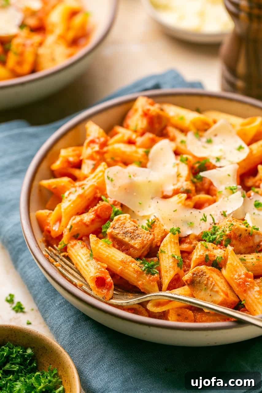 a side view of a bowl of chicken and penne vodka topped with parsley