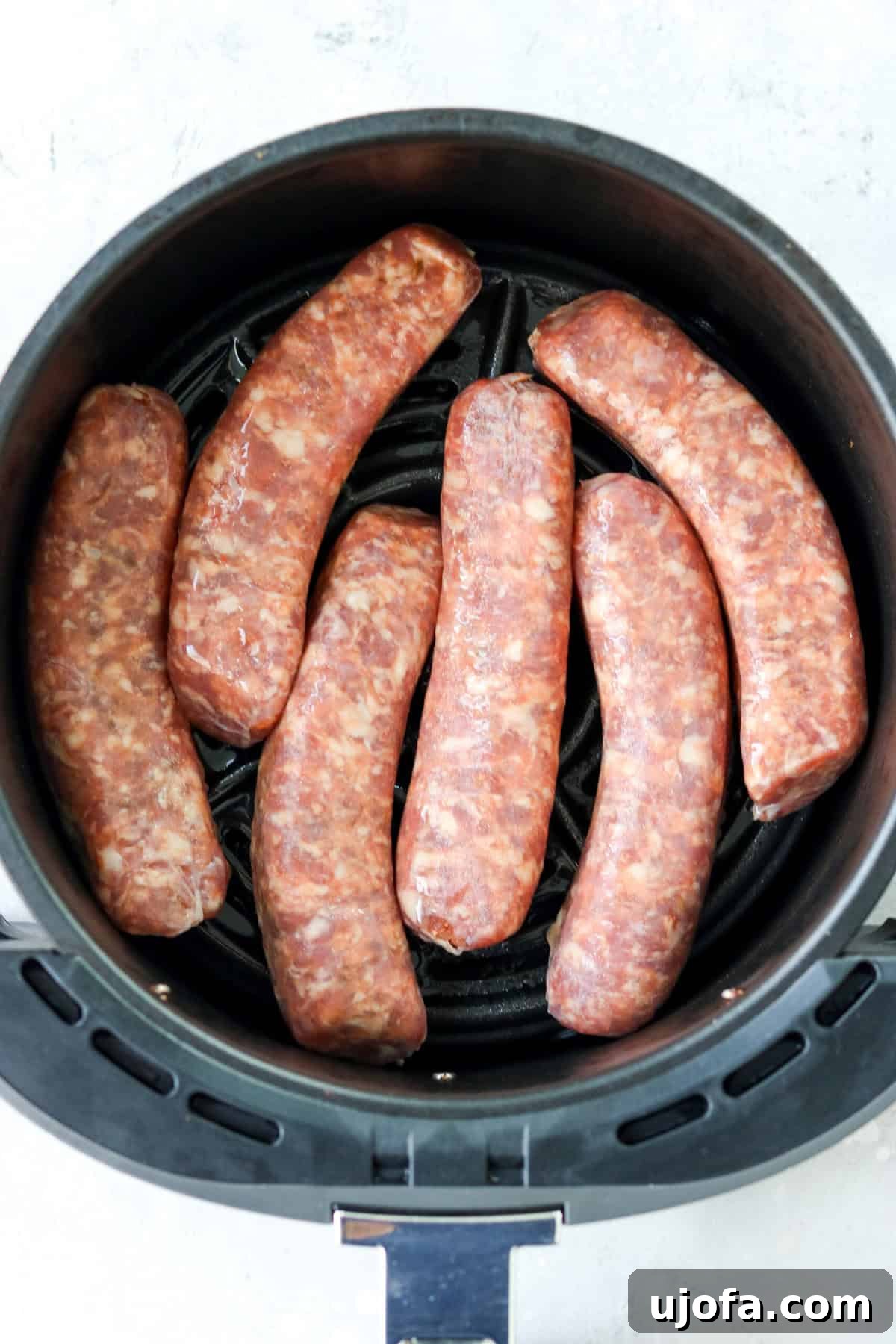 Quick and Crispy Air Fryer Italian Sausage 4 Raw Italian sausages neatly arranged in a single layer within an air fryer basket, ready for cooking.