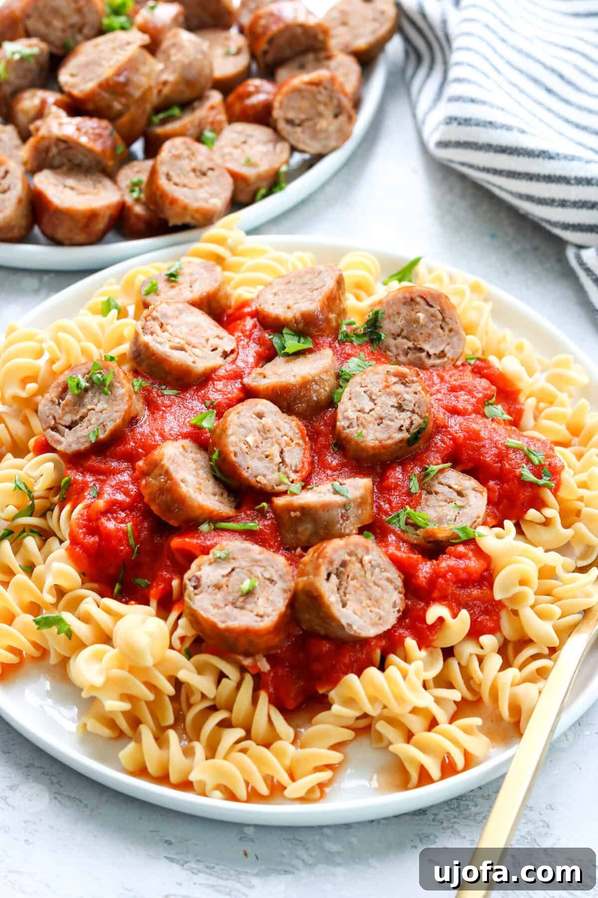 Quick and Crispy Air Fryer Italian Sausage 7 A beautifully plated dish featuring pasta with marinara sauce and sliced Italian sausage, with more sausages in the background.