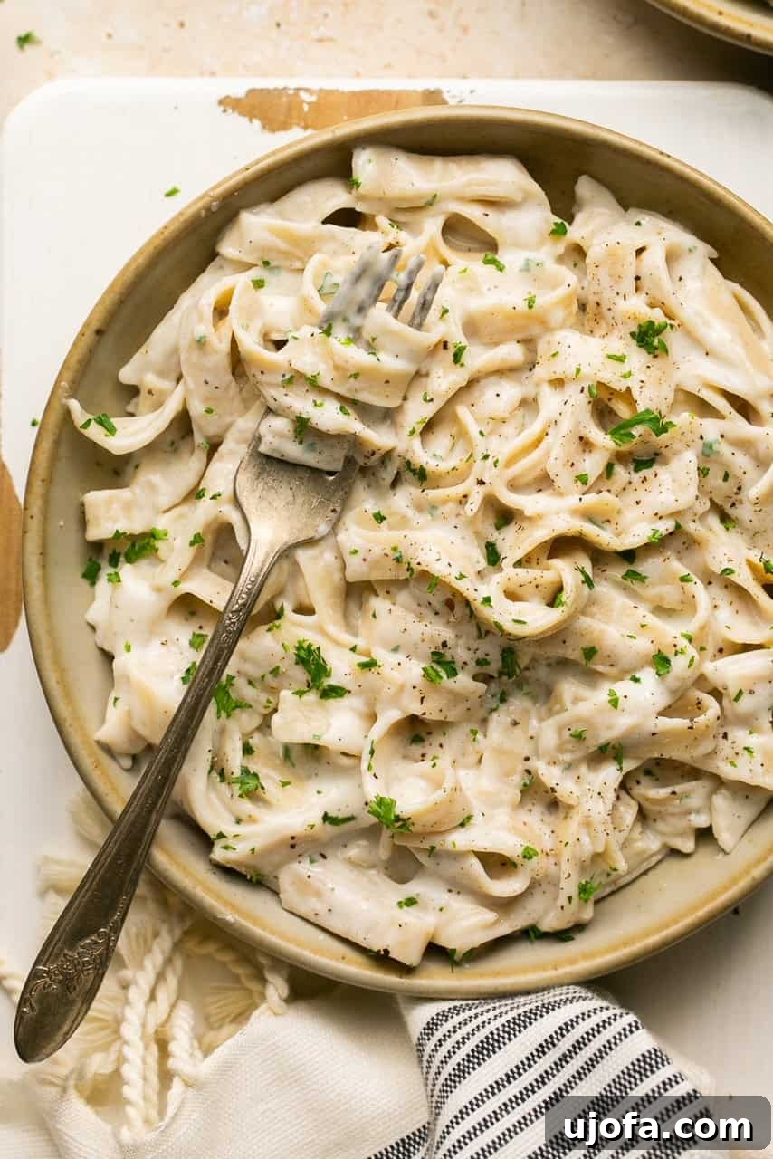 A delectable bowl of tagliatelle pasta generously coated with creamy Cottage Cheese Alfredo sauce, garnished with fresh parsley and ready to be enjoyed with a fork.