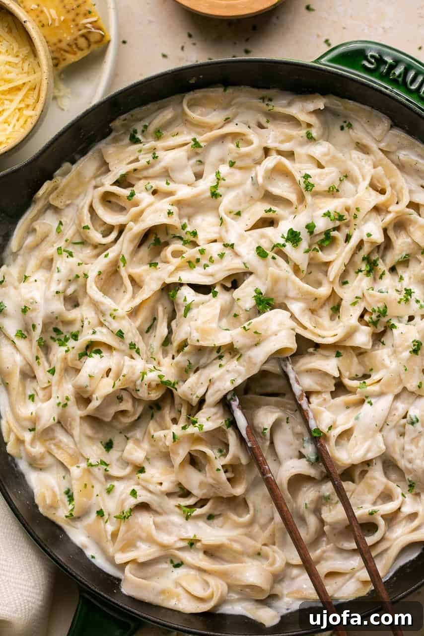 Freshly made Cottage Cheese Alfredo pasta in a cast iron skillet, being tossed with tongs, highlighting its creamy texture.
