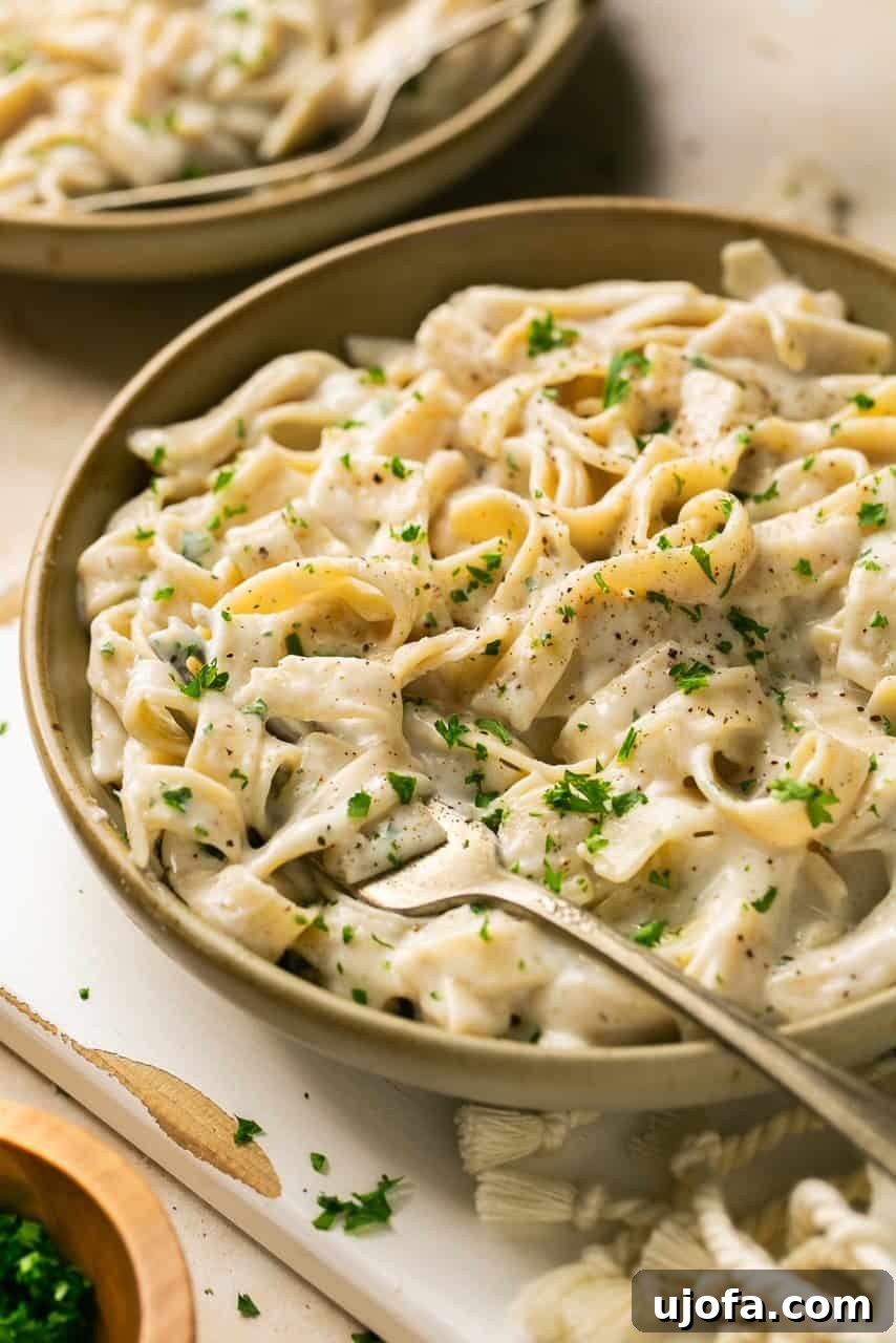 A close-up of a bowl of creamy Cottage Cheese Alfredo pasta, topped with vibrant fresh parsley and a fork, ready to be eaten.