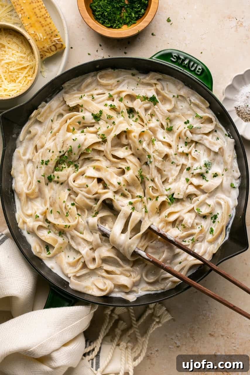 A vibrant green and black skillet filled with creamy Cottage Cheese Alfredo pasta, with tongs poised to serve.