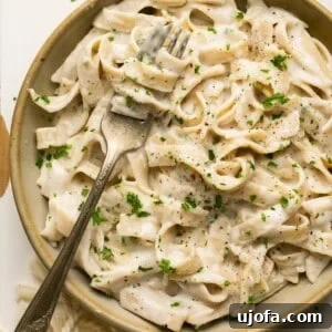 tagliatelle pasta with alfredo sauce in a bowl with a fork topped with parsley