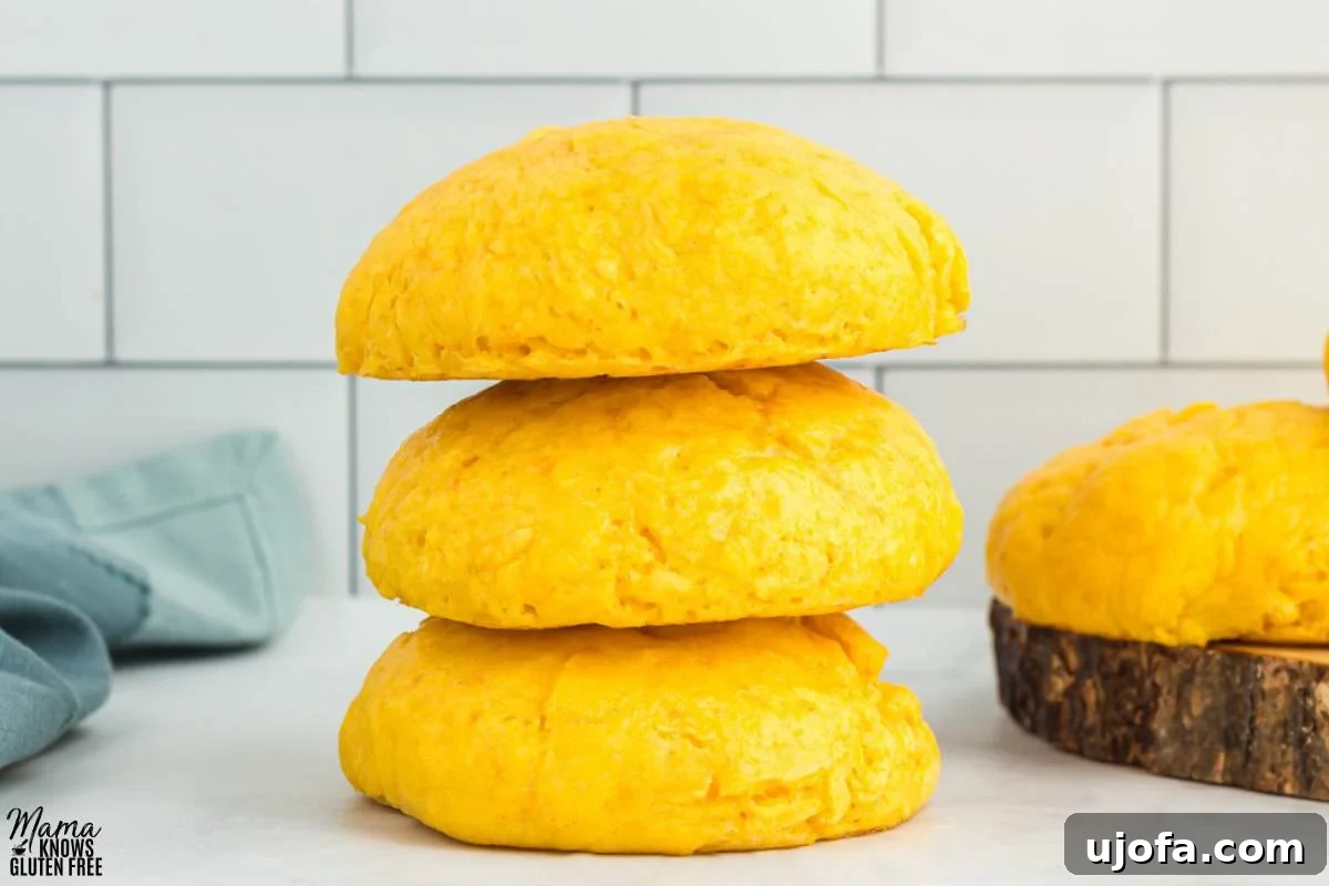 A pile of three Gluten-Free Sweet Potato Rolls on kitchen counter with towel and another roll in the background.