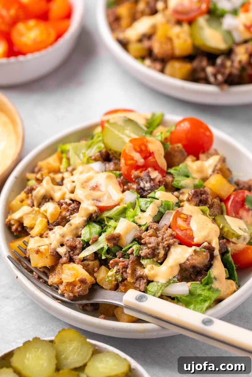 A hearty bowl of homemade Big Mac Casserole, garnished with fresh lettuce, tomatoes, pickles, and a swirl of special sauce, with a wooden fork resting in it.