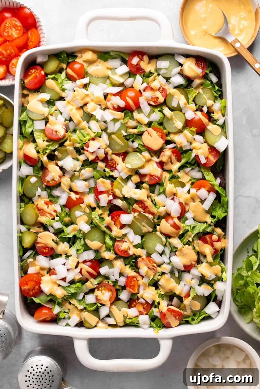 A fully assembled Big Mac Casserole in a baking dish, showcasing layers of potatoes, ground beef, melted cheese, and fresh toppings drizzled with special sauce.