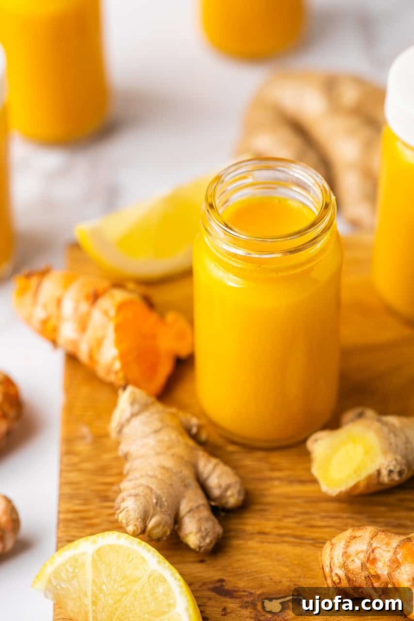 Power-Packed Lemon Ginger Turmeric Shots for Immunity 2 Lemon ginger turmeric shot in a small glass jar on a wooden cutting board with fresh ginger around it.