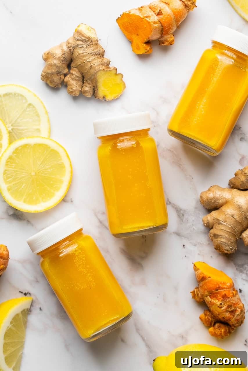 Power-Packed Lemon Ginger Turmeric Shots for Immunity 5 Lemon ginger turmeric shots with white screw-on lids laying next to lemon slices, ginger, and turmeric
