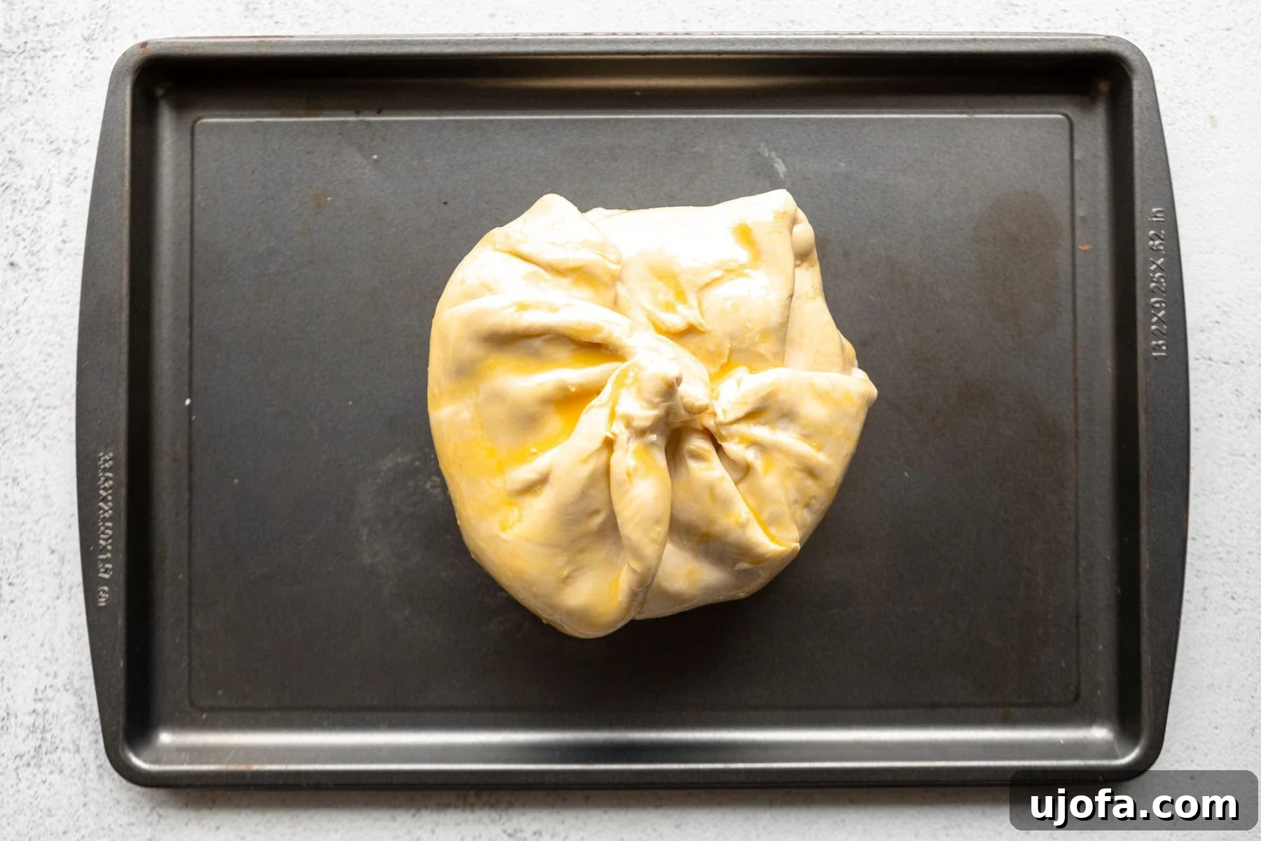 Unbaked gluten-free baked brie brushed with egg wash on a baking sheet.