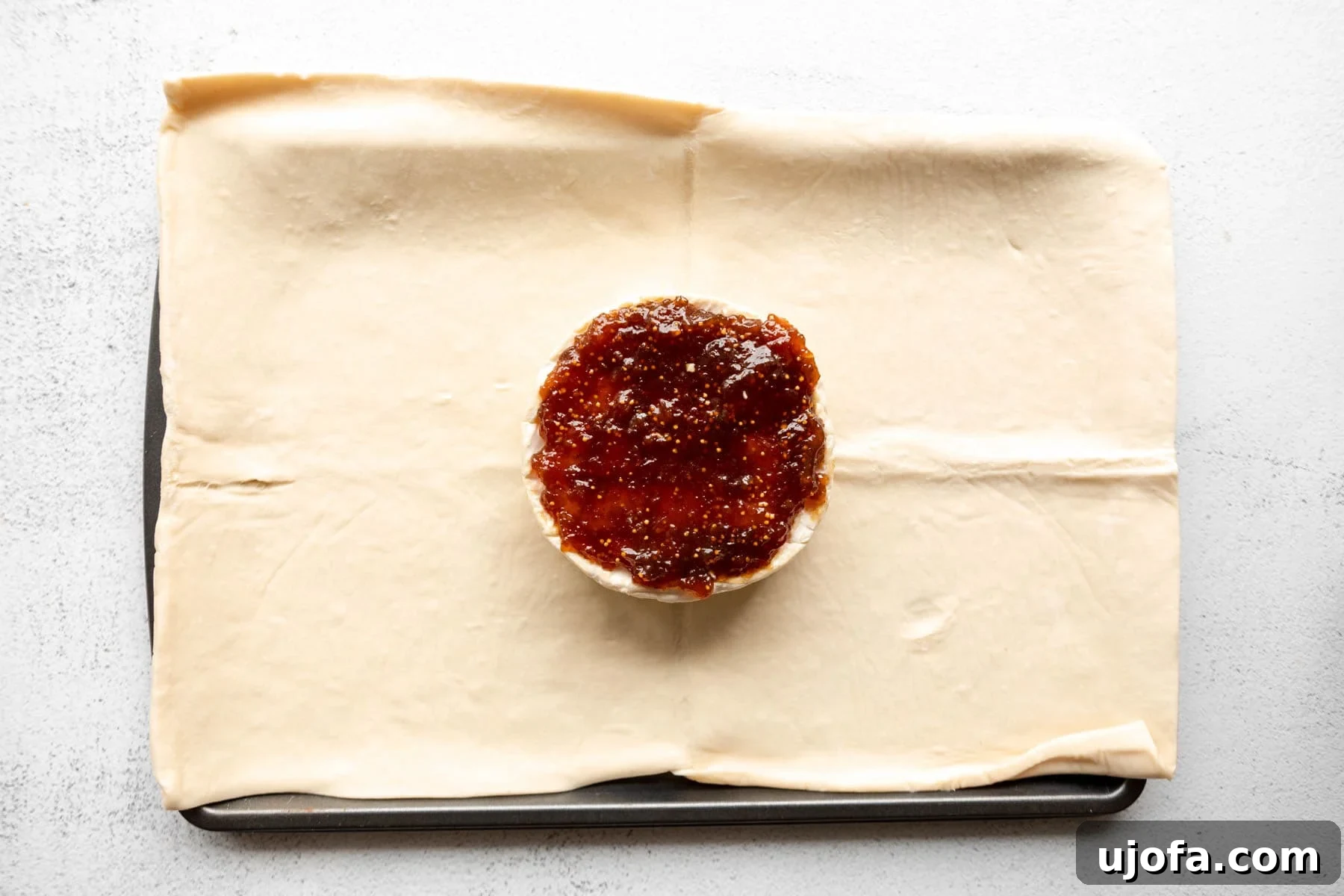 A wheel of brie topped with fig jam on a sheet of gluten-free puff pastry.