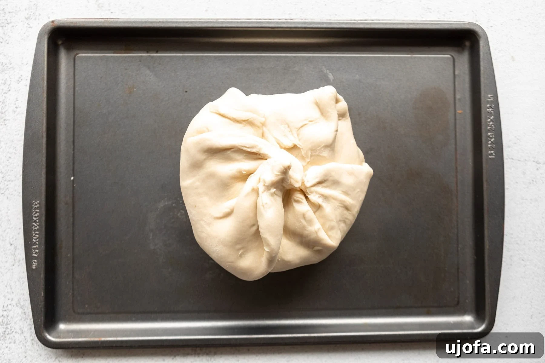 A wheel of brie wrapped in gluten-free puff pastry dough on a baking sheet.