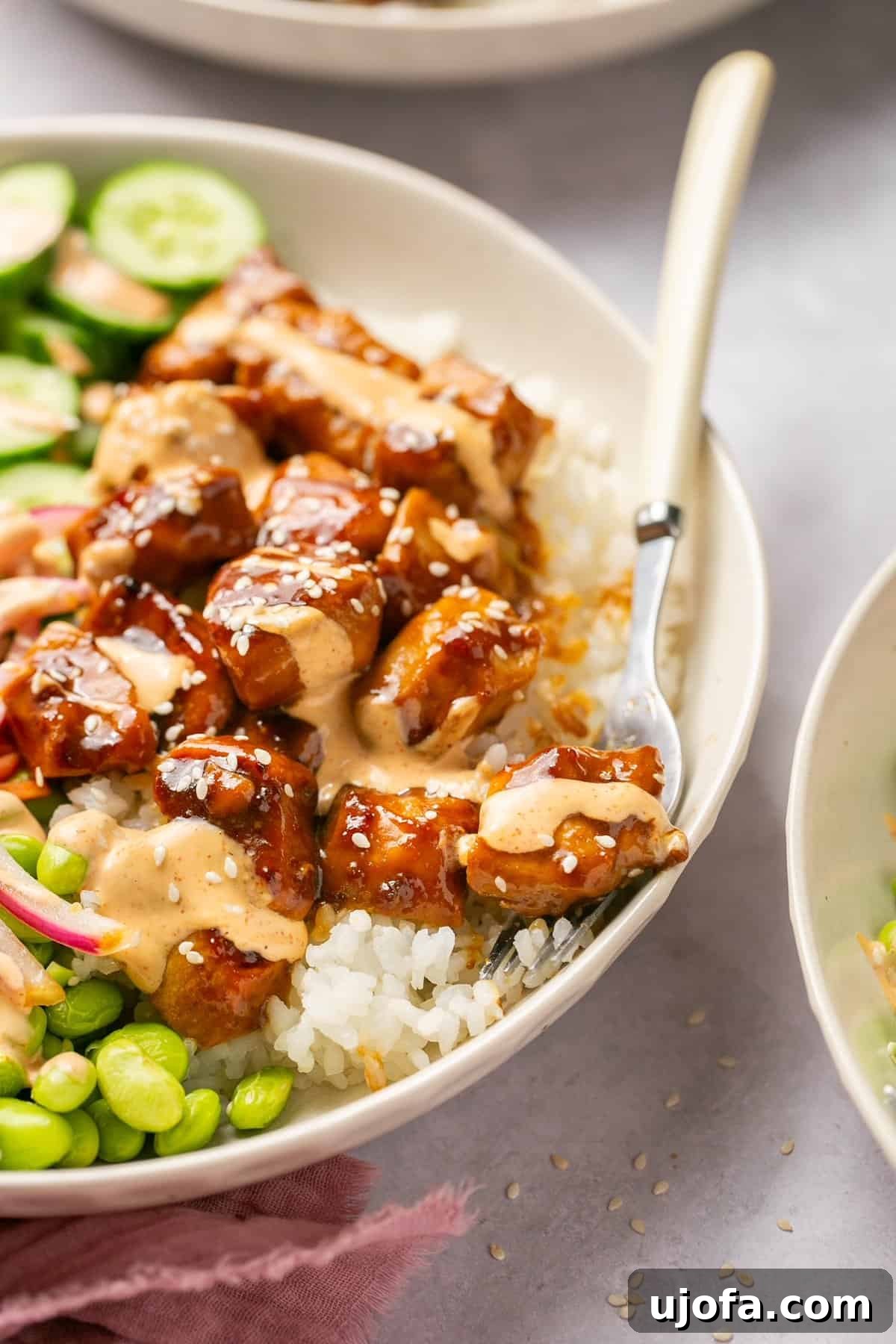 Sweet & Spicy Teriyaki Chicken Poke Bowls 8 a fork taking a bite of chicken out of a bowl