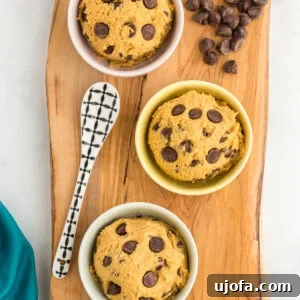 Three small, inviting bowls of edible chickpea cookie dough, generously topped with chocolate chips, artfully arranged on a wooden serving board alongside a decorative spoon and scattered chocolate chips.