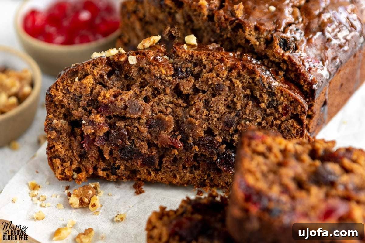 Sumptuous Gluten-Free Fruitcake 2 Close up of a slice of Gluten-Free Fruit Cake with candied cherries in the background, showcasing its rich texture.