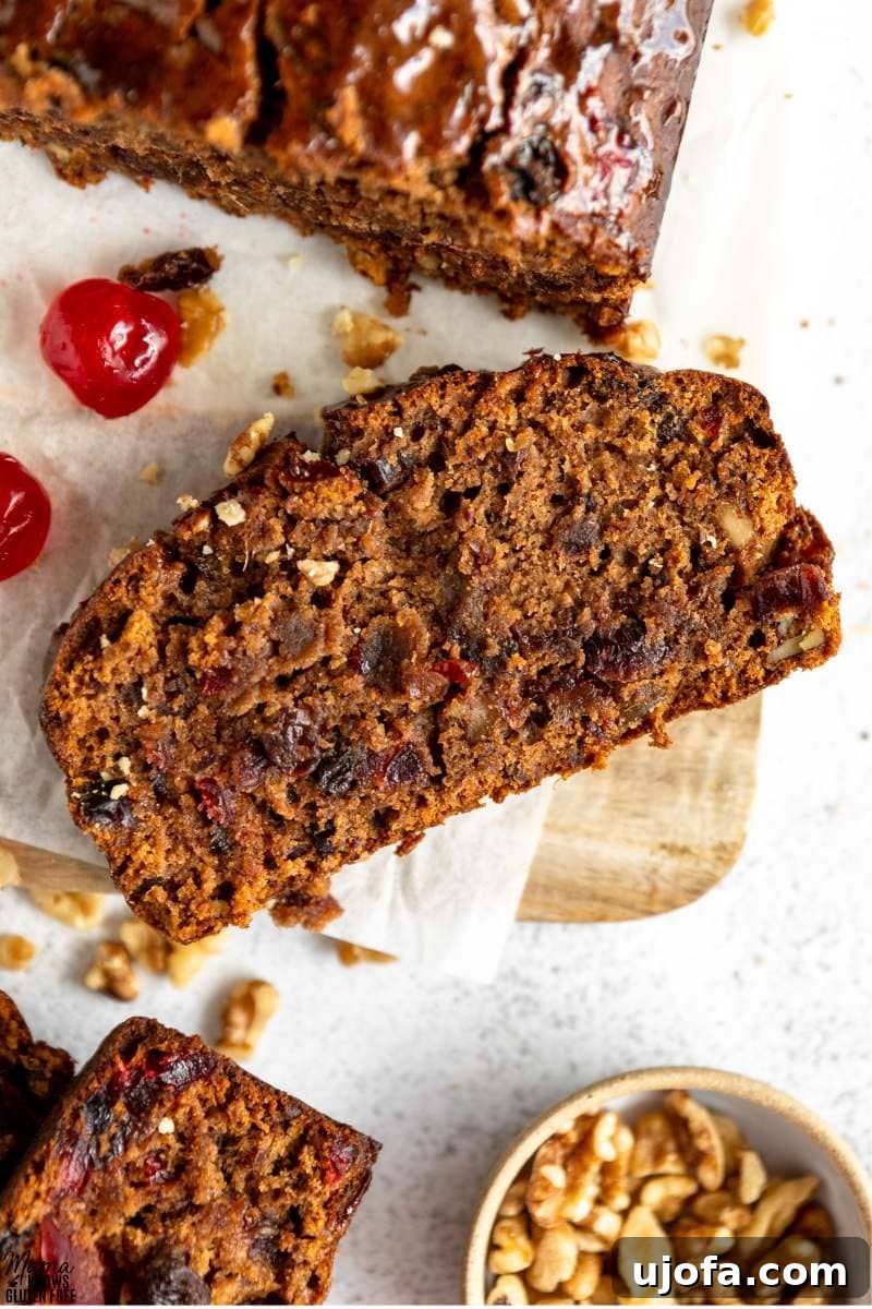 Sumptuous Gluten-Free Fruitcake 4 Overhead shot of a slice of Gluten-Free Fruit Cake on parchment paper and wooden board, showing its generous fruit and nut content.