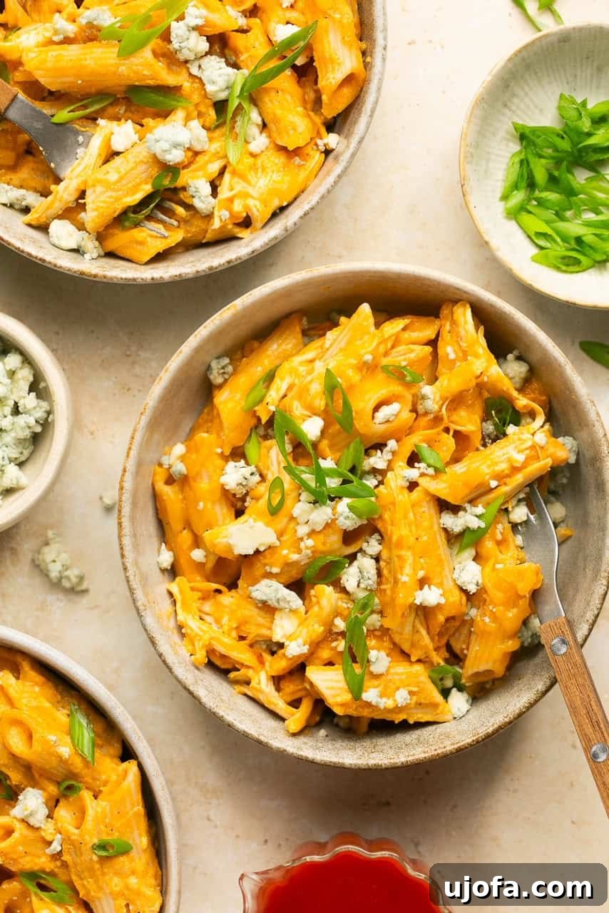 two bowls of buffalo chicken pasta topped with blue cheese crumbles and green onions