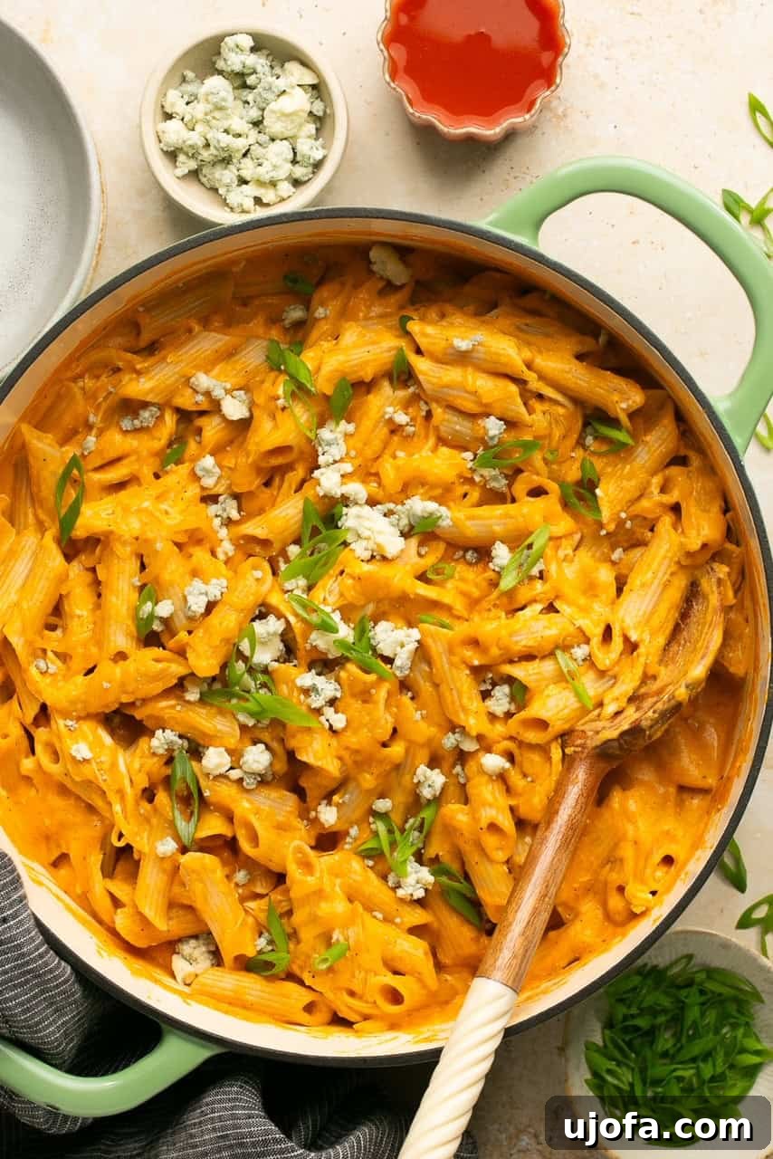 buffalo chicken pasta in a green skillet with a wooden spoon resting on the side