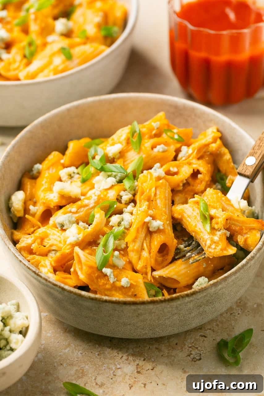 a close up of a bowl of buffalo chicken pasta topped with blue cheese crumbles and green onions