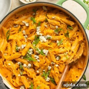 cheesy buffalo chicken pasta in a green pot topped with green onion and blue cheese crumbles