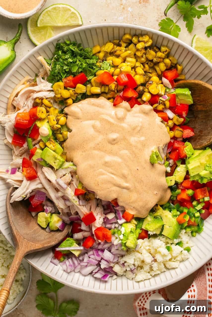 The creamy cilantro lime dressing poured over the mixed salad ingredients in a bowl before tossing.