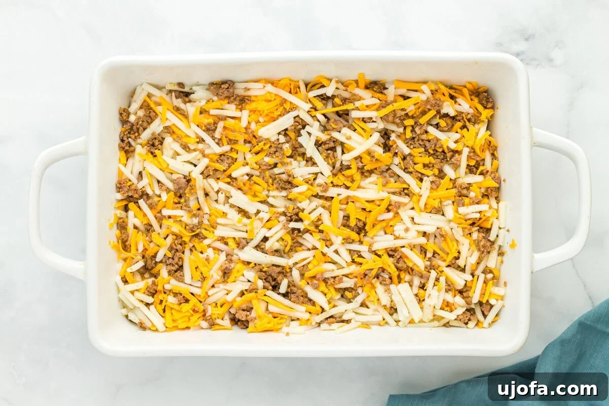 hash browns, cheese, and crumbled cooked sausage in a baking pan.