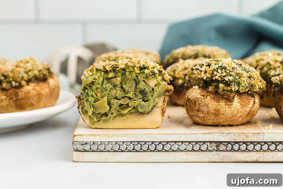 Wholesome Mushroom Poppers 4 A gluten-free stuffed mushroom sliced in half on a chopping board with other stuffed mushrooms.