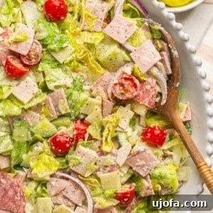 Italian grinder salad in a white bowl with a wooden spoon