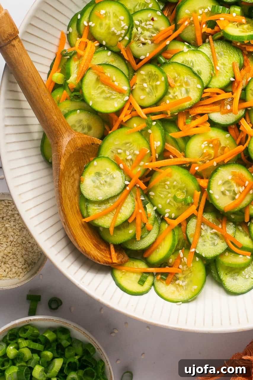 Refreshing Cucumber Carrot Crunch 2 A vibrant bowl of freshly sliced cucumbers and shredded carrots, generously topped with sesame seeds. A rustic wooden spoon rests gently on the side of the bowl, inviting you to dive into this refreshing salad.
