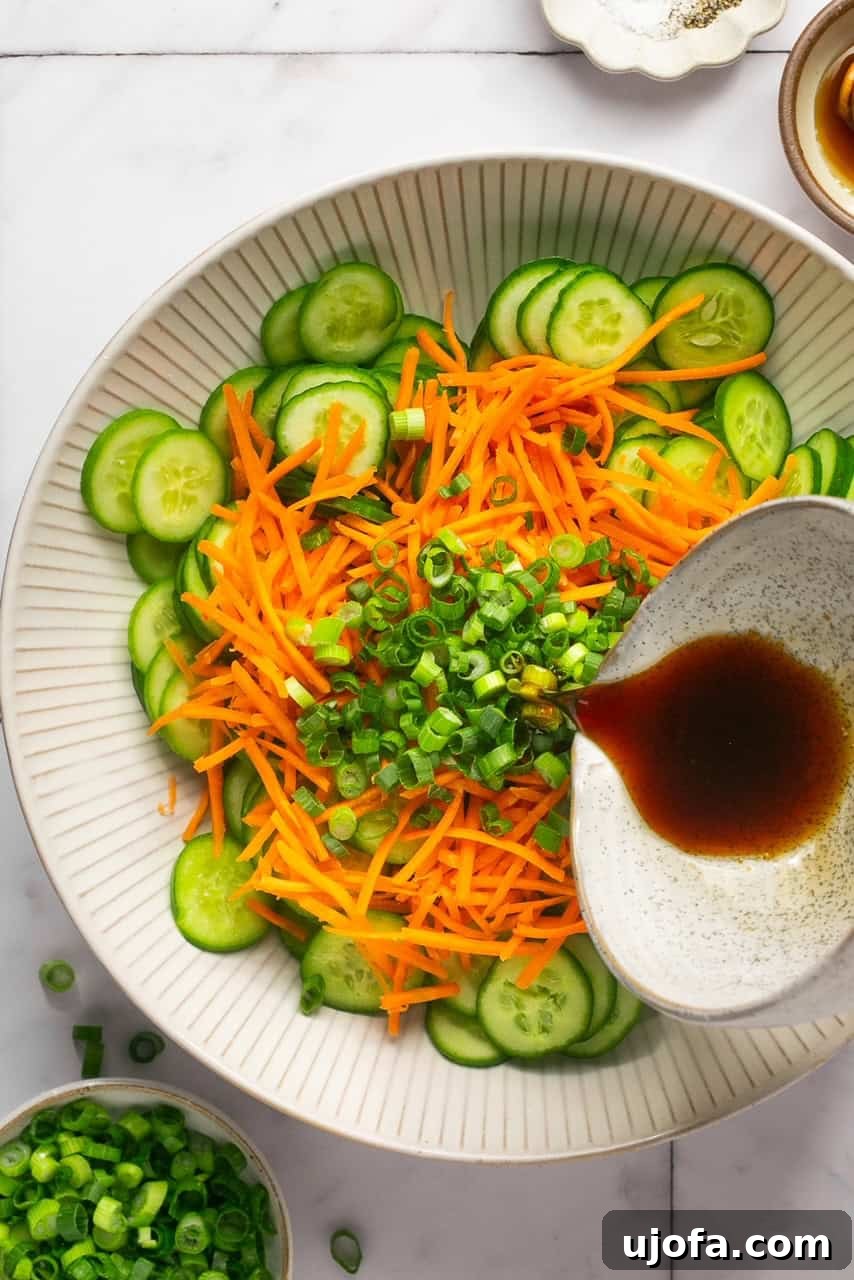 Refreshing Cucumber Carrot Crunch 5 A close-up shot capturing the moment a glossy Asian-inspired dressing is poured elegantly over a bowl brimming with crisp cucumber and carrot slices. The scene highlights the vibrant colors of the fresh vegetables as they become coated in the rich, aromatic sauce.