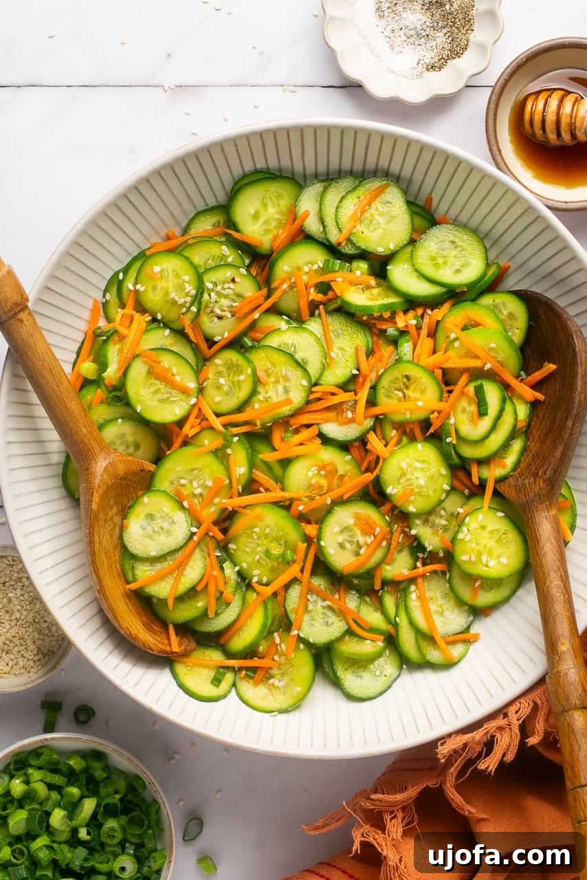 Refreshing Cucumber Carrot Crunch 6 A close-up of a refreshing cucumber carrot salad in a large, elegant white bowl, garnished with sesame seeds. Two rustic wooden spoons rest neatly on the rim, ready for serving.