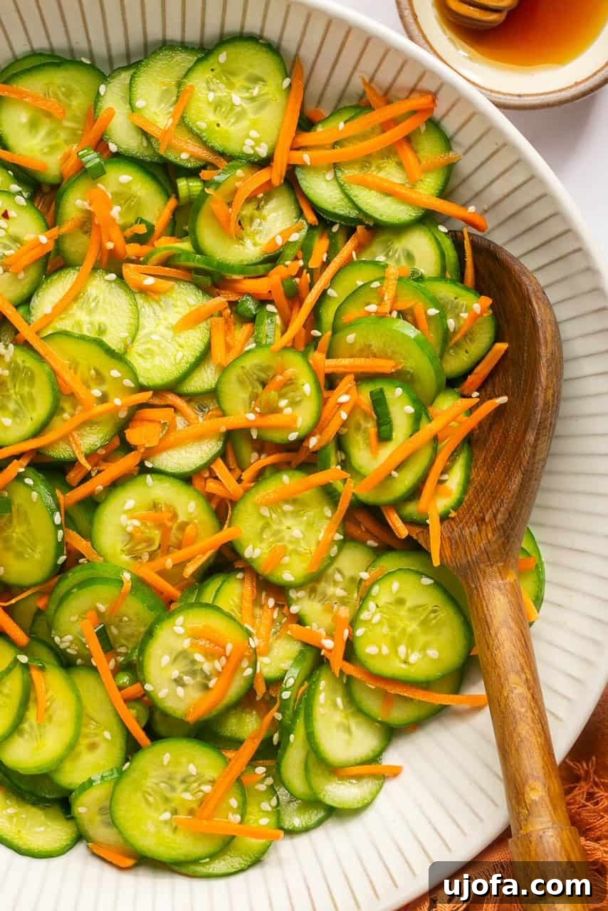 Refreshing Cucumber Carrot Crunch 7 A vibrant, close-up view of a crunchy cucumber carrot salad, freshly tossed and glistening with dressing, showcased in a large white serving bowl with a wooden spoon nestled within, inviting a delicious bite.
