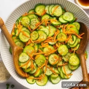 Refreshing Cucumber Carrot Crunch 8 A beautifully presented cucumber carrot salad in a white bowl, accentuated with two wooden spoons resting on the side, inviting you to enjoy its crisp texture.