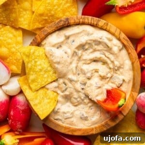cottage cheese queso in a wooden bowl surrounded by tortilla chips and peppers with some dipped in the middle