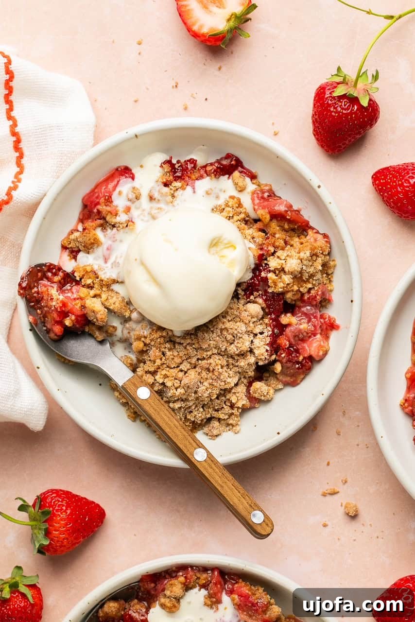 Sweet & Simple Gluten-Free Strawberry Crumble 8 An inviting overhead shot of a freshly baked strawberry crumble, portioned onto a white plate with a spoon resting alongside, ready for a delightful dessert experience.