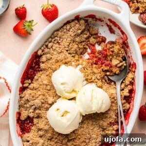 Sweet & Simple Gluten-Free Strawberry Crumble 9 strawberry crumble in an oval baking dish topped with 3 scoops of vanilla ice cream with a spoon taking a portion out