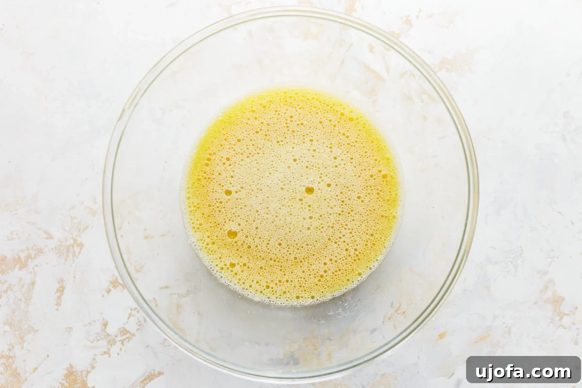 Grain-Free Almond Loaf 5 A clear glass bowl holding a vibrant blend of wet ingredients for almond flour bread, including whisked eggs, applesauce, olive oil, water, honey, and apple cider vinegar, gleaming with freshness.