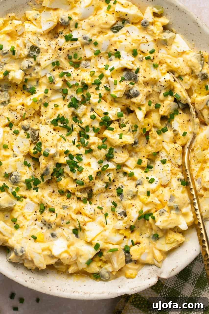 A close-up shot of vibrant dill pickle egg salad in a rustic white bowl, garnished with fresh dill.