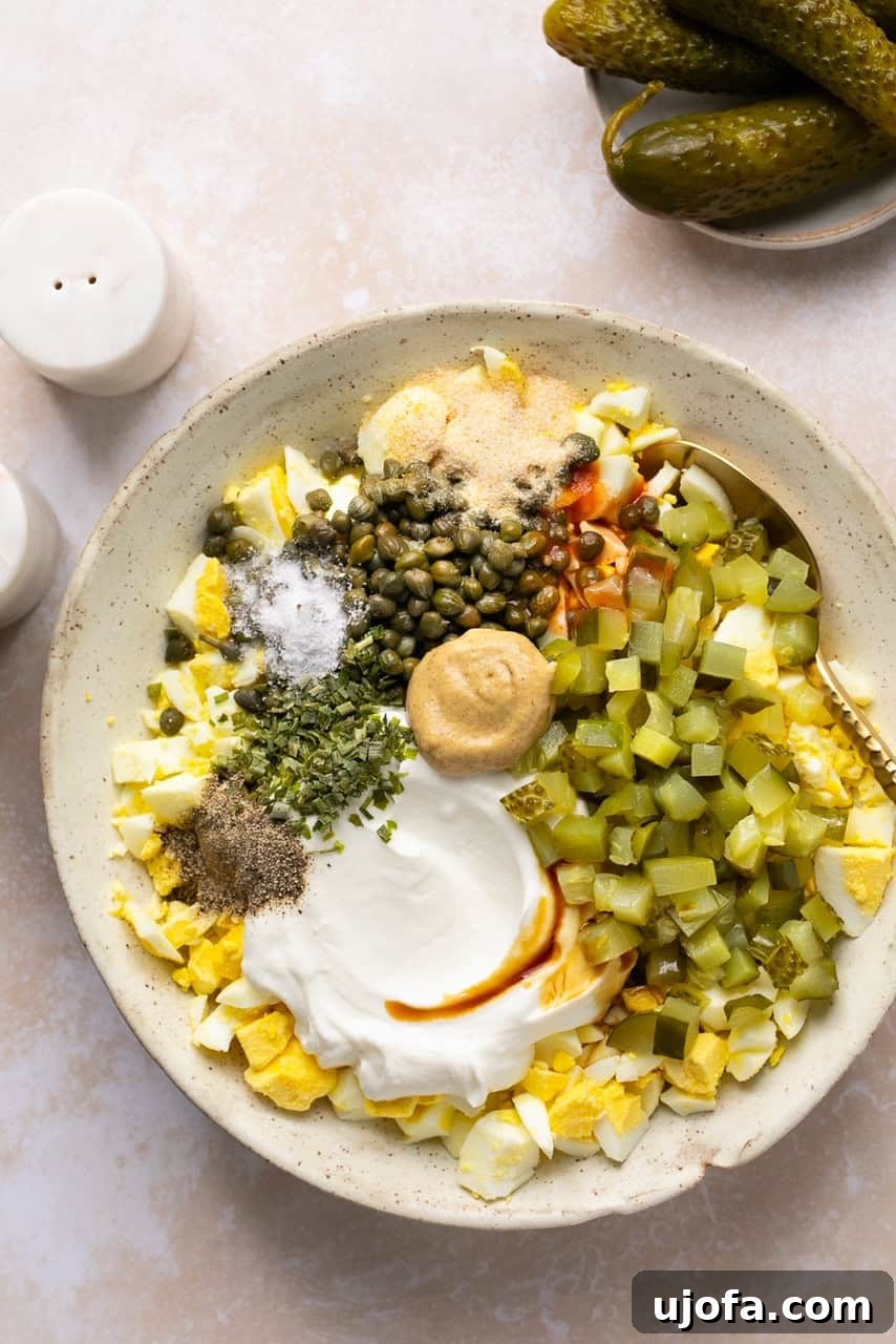 A large mixing bowl containing chopped hard-boiled eggs and various dressing ingredients, ready to be combined for the dill pickle egg salad.