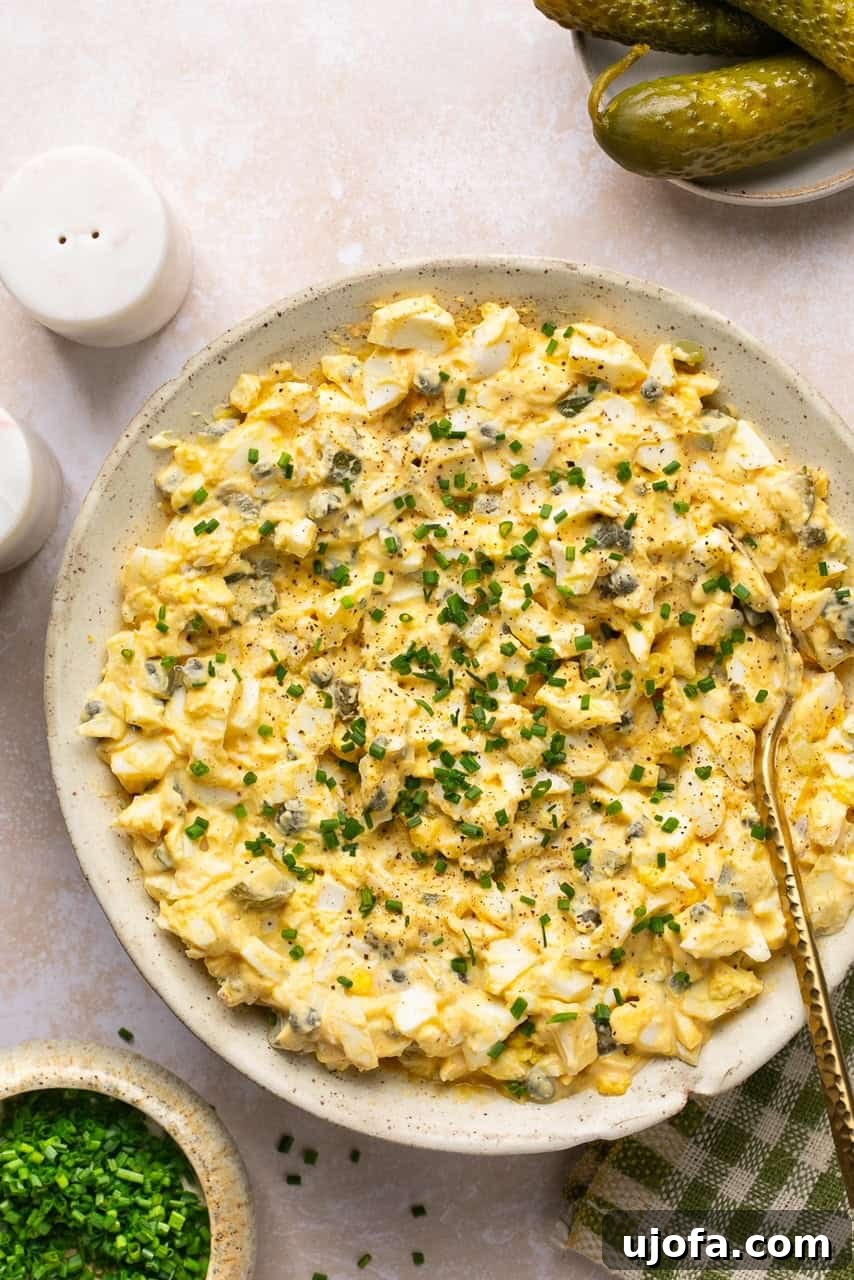 A close-up of dill pickle egg salad in a bowl, garnished with fresh chopped chives, highlighting its readiness to serve.
